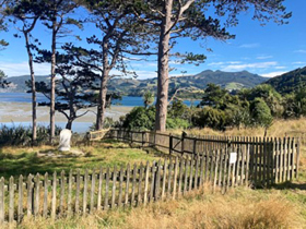 a fence around an old cemetery and trees with the sea and mountains in the background