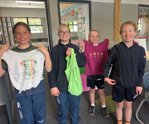 four children holding up their t-shirts in a classroom