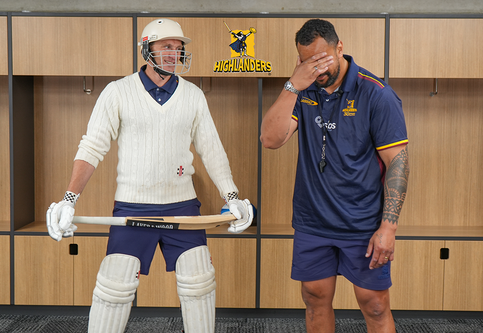 a person in a rugby changing room wearing a cricket uniform and a rugby player shaking his head