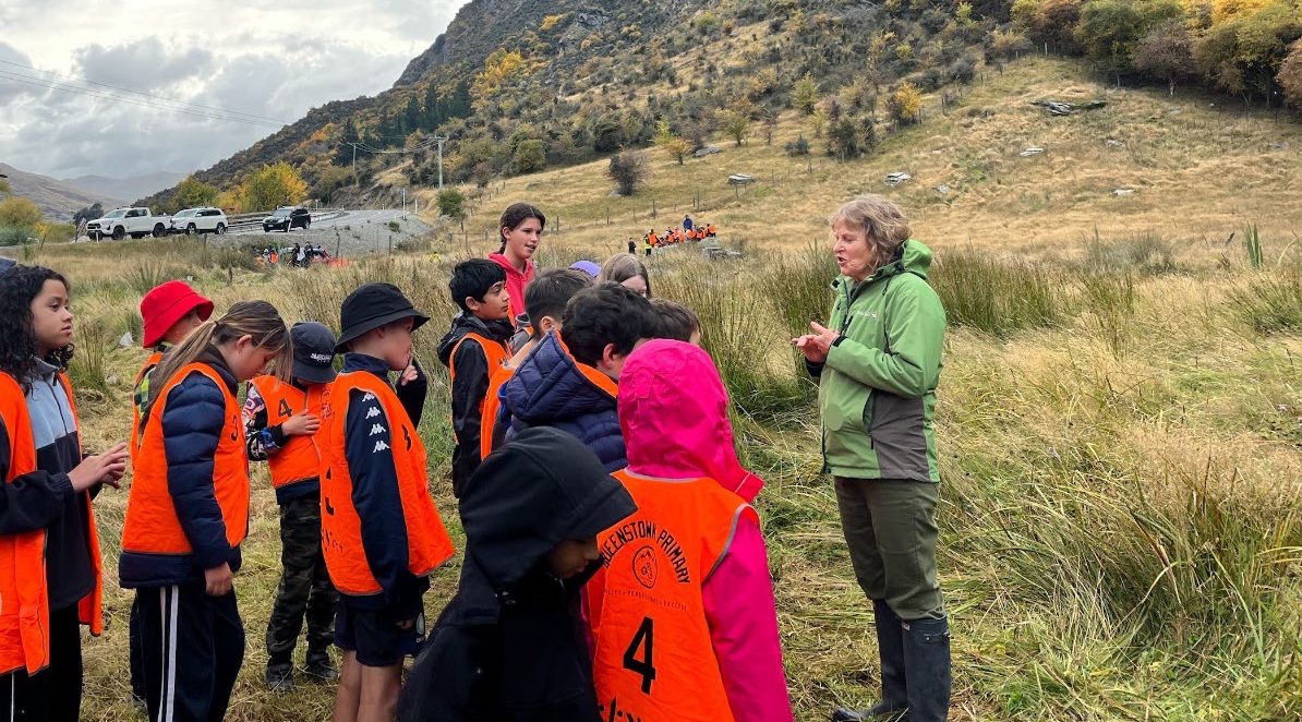 a group of children standing in a field with an adult who is talking to them