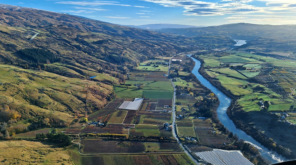 an aerial view of a rural valley with paddocks, some buildings, and a river running through it