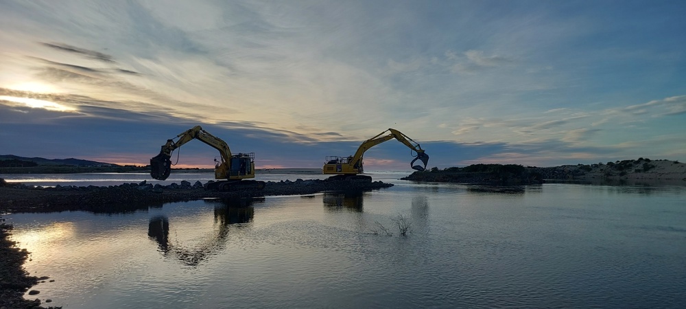 Two large diggers on top of rock walls beside Puerua River
