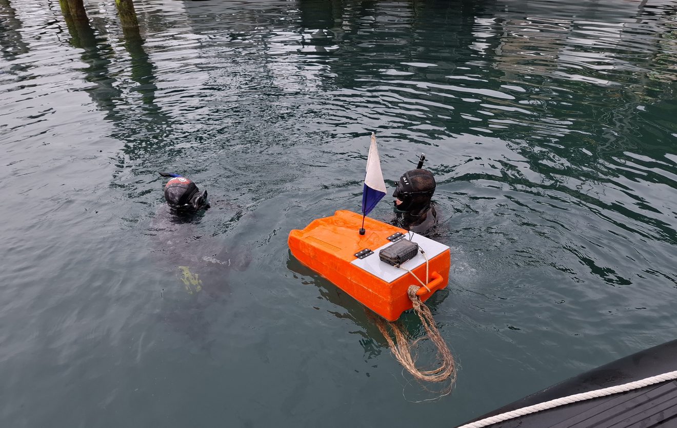 two people diving in the water with an orange piece of equipment floating on the water beside them