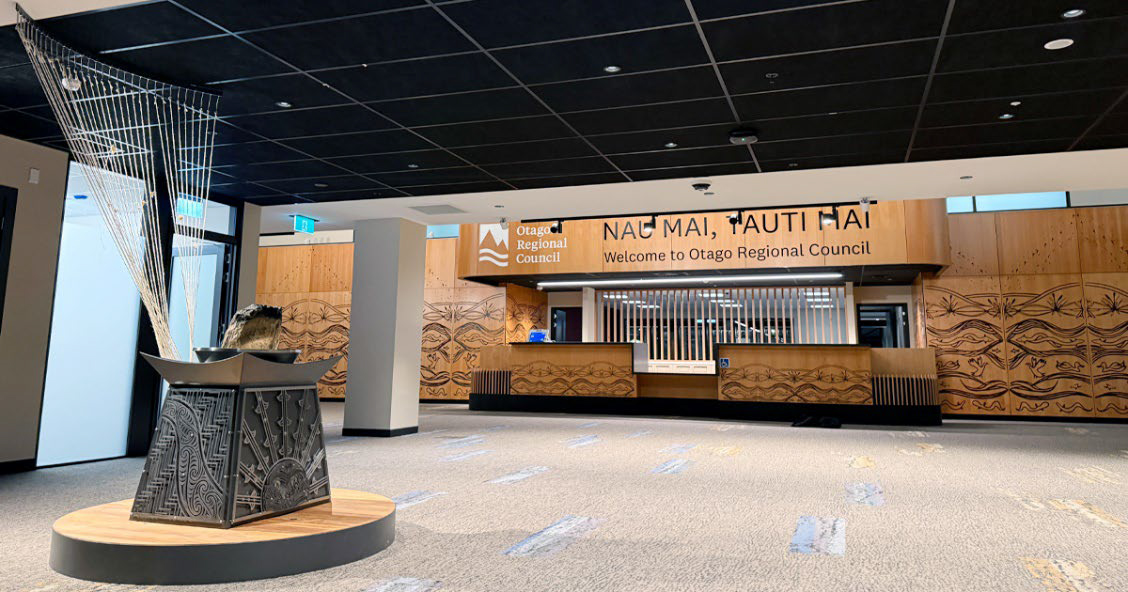 the entrance to a building, with a sculpture in front and a reception desk behind it