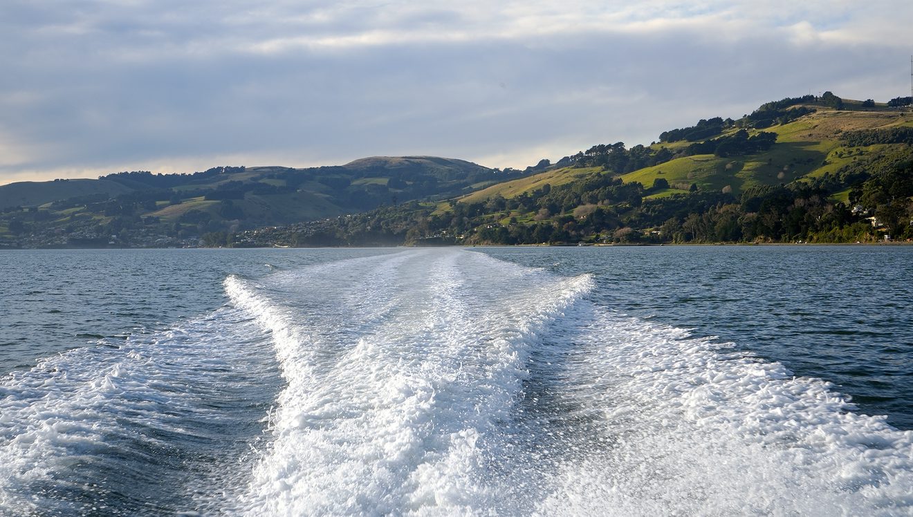 the wake of a boat on a harbour with mountains in the background
