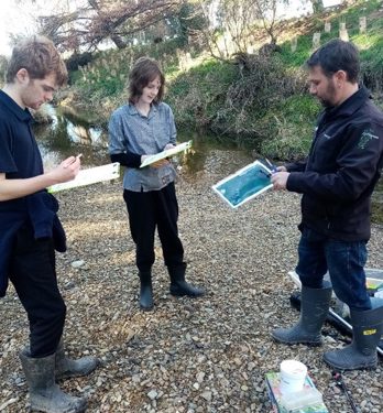 Three people standing in a creek bed looking at clipboards