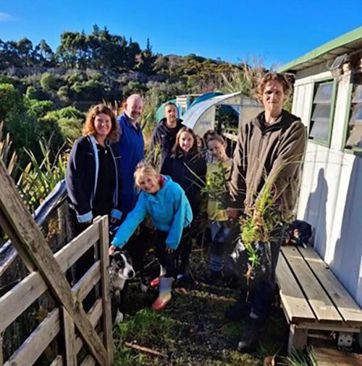 a group of people and a dog standing outside a small building with bush in the background