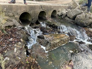 three culverts side by side with water flowing into a river, the concrete is crumbling with sharp drops to the water