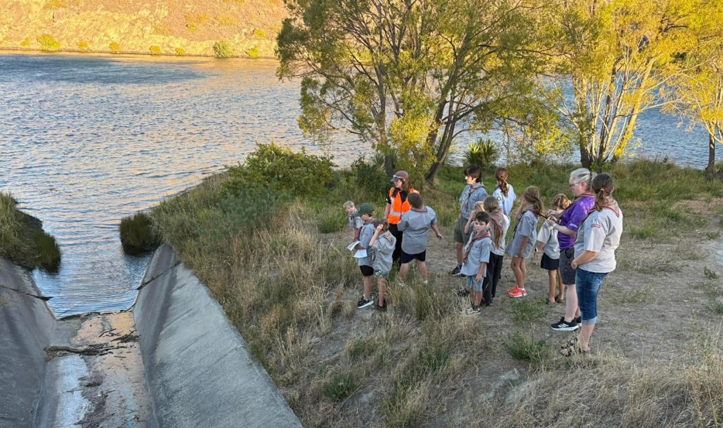 a group of children in scout uniforms standing beside an open drain that runs into a waterway