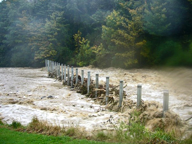a swollen river with a debris trap running from one side to the other. The trap has lots of branches and other material stuck in it