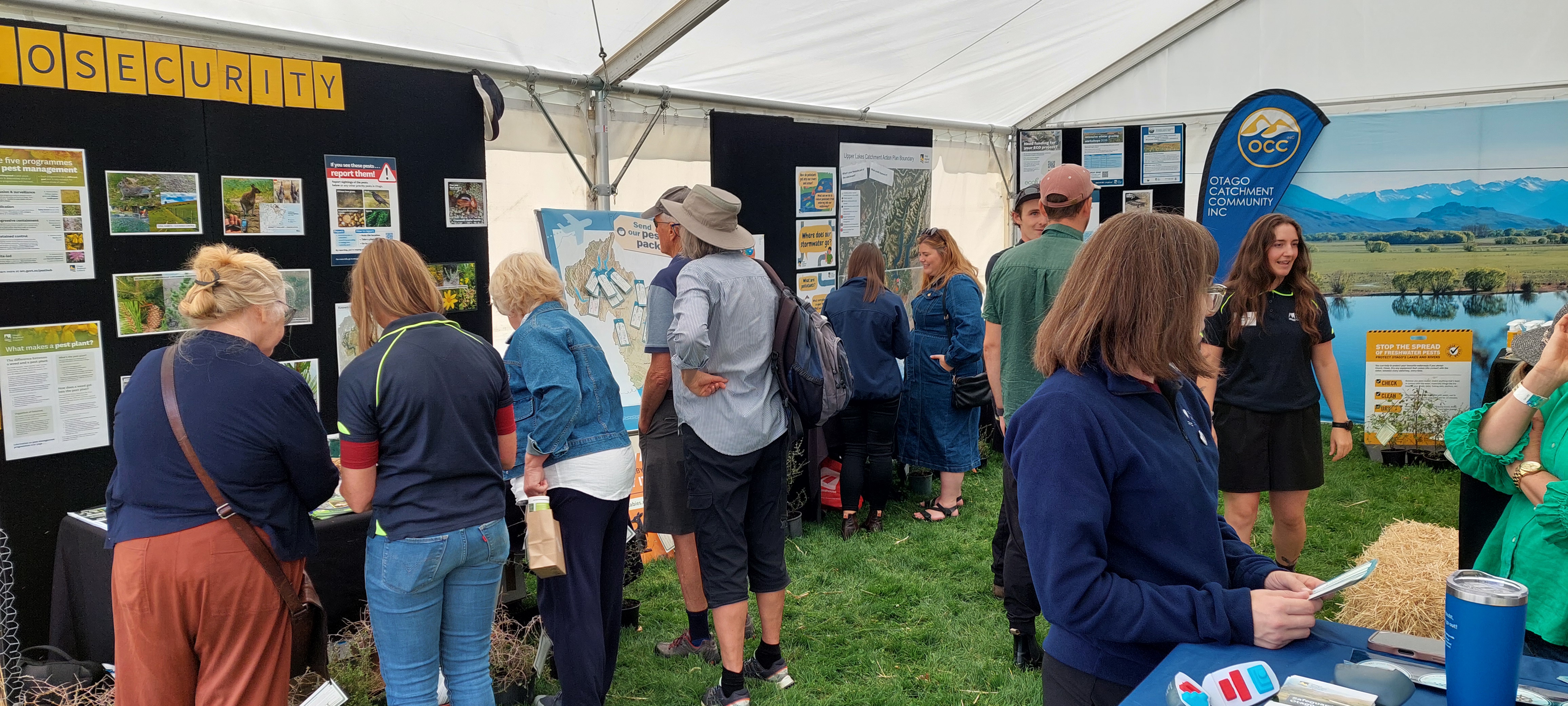 a group of people inside a large tent that has displays and posters around the walls. The people are looking at things and talking to other people