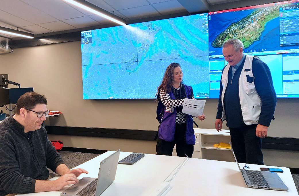 three people in a room with large screens behind them with maps showing