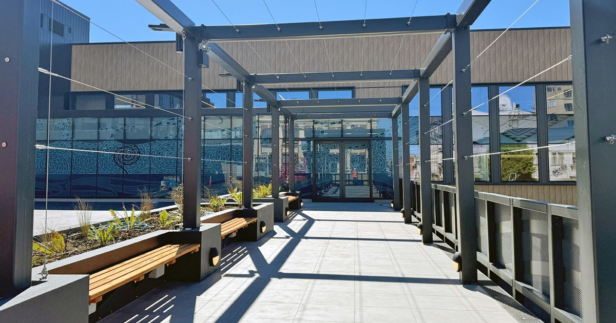 a walkway into a building with benches and plants on it