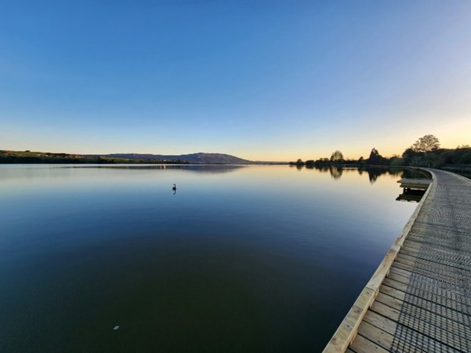 a view of a lake with a boardwalk track running alongside it at sunset
