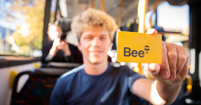 a young person on a bus holding a Bee Card towards the camera and smiling