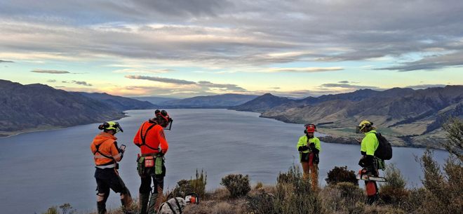 a group of people standing on top of a mountain overlooking Hunter Valley Station, above Lake Hāwea