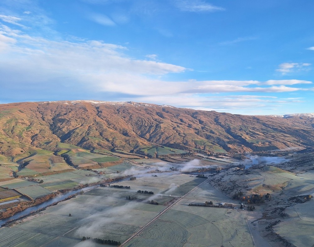 an aerial view of a valley with mountains in the background and a blue sky