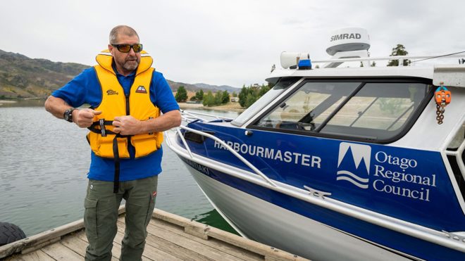 a person standing on a wharf beside a boat and putting on a lifejacket