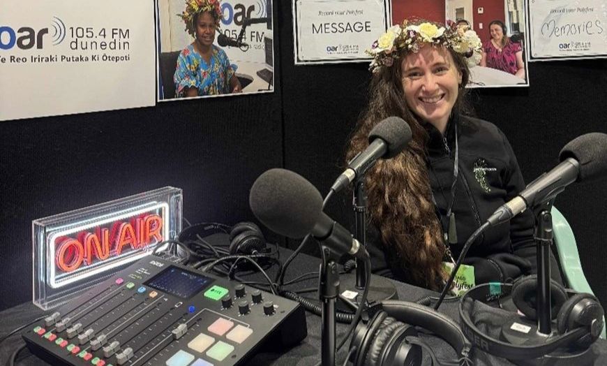 a person sitting beside radio equipment smiling at the camera with a wreath of colourful flowers in their hair