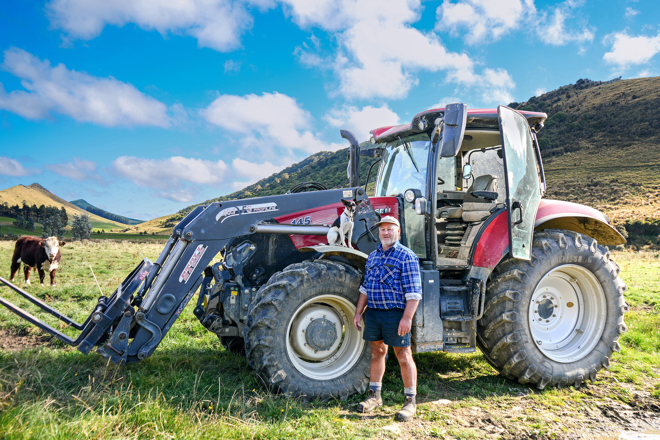 a person standing in front of a tractor in a field with a small dog on the tractor