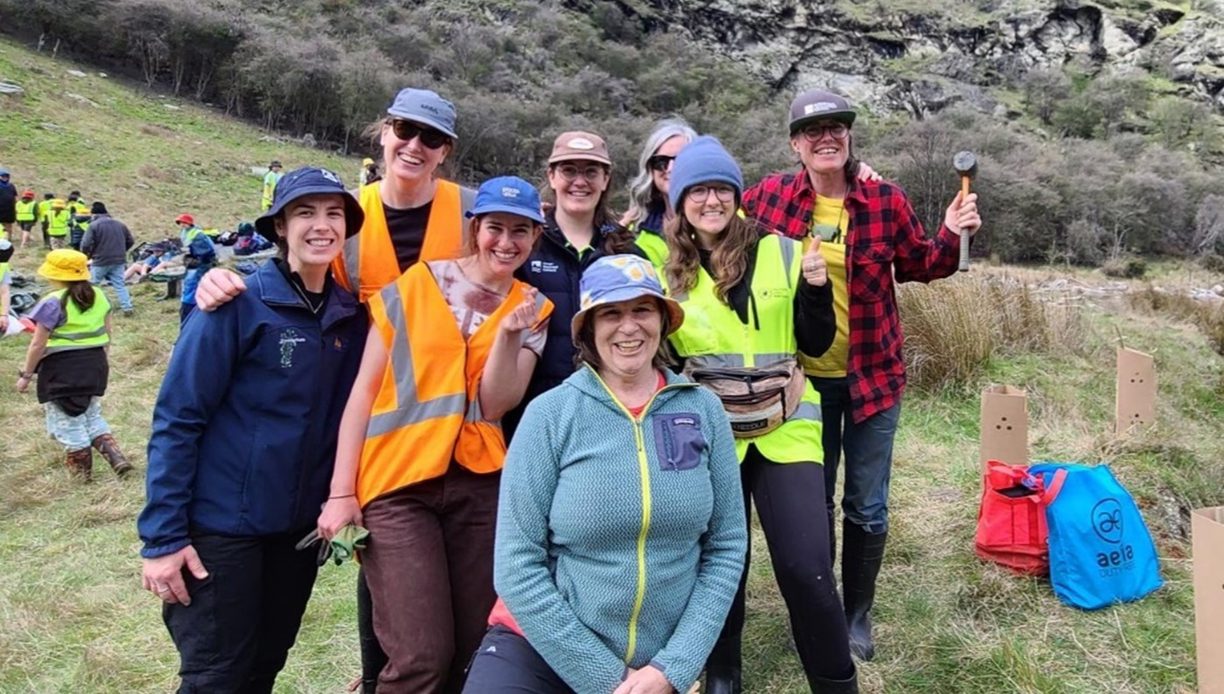 a group of smiling people looking at the camera standing outside in a paddock with plants and rocks behind them
