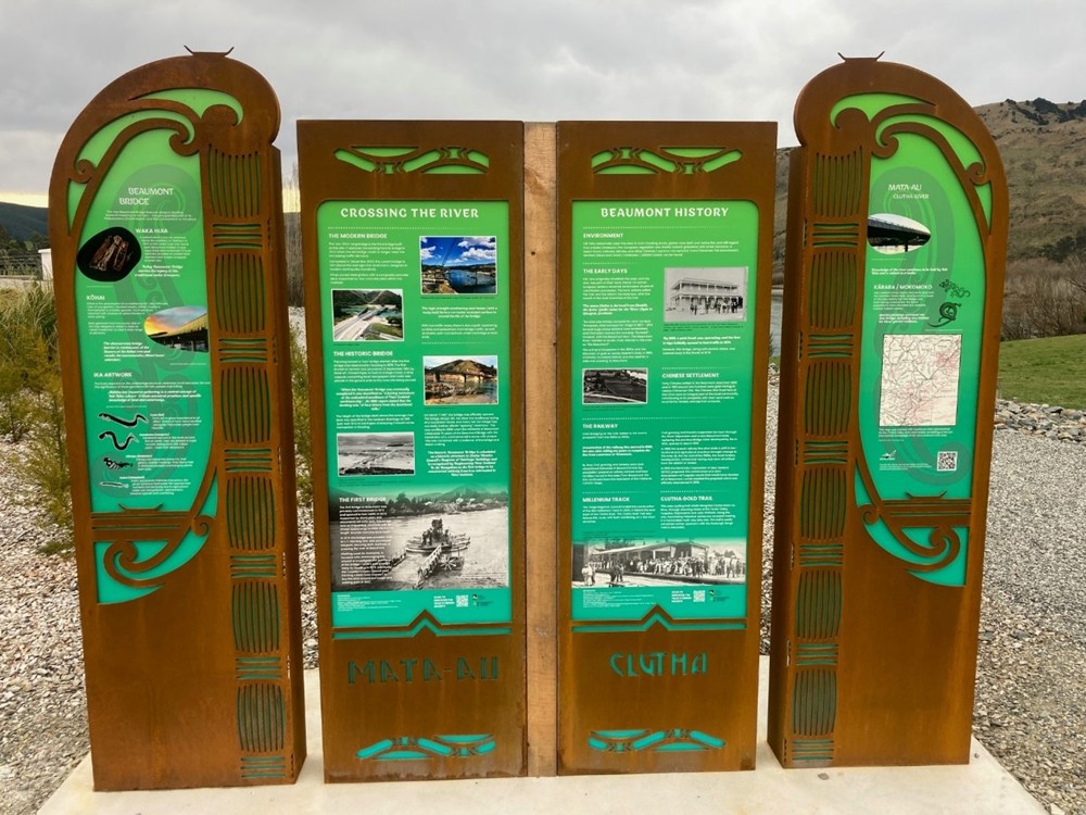 a four-panelled sign outdoors with grass and hills behind it