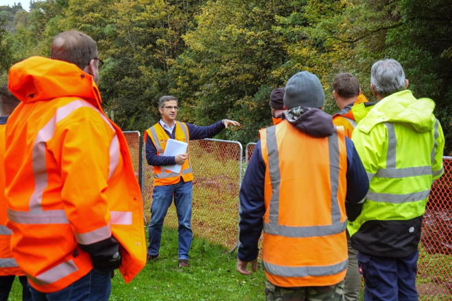 a group of people in orange vests talking to a man standing beside a fenced-off waterway