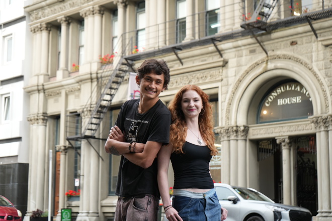 two young people standing side-by-side in front of an old building