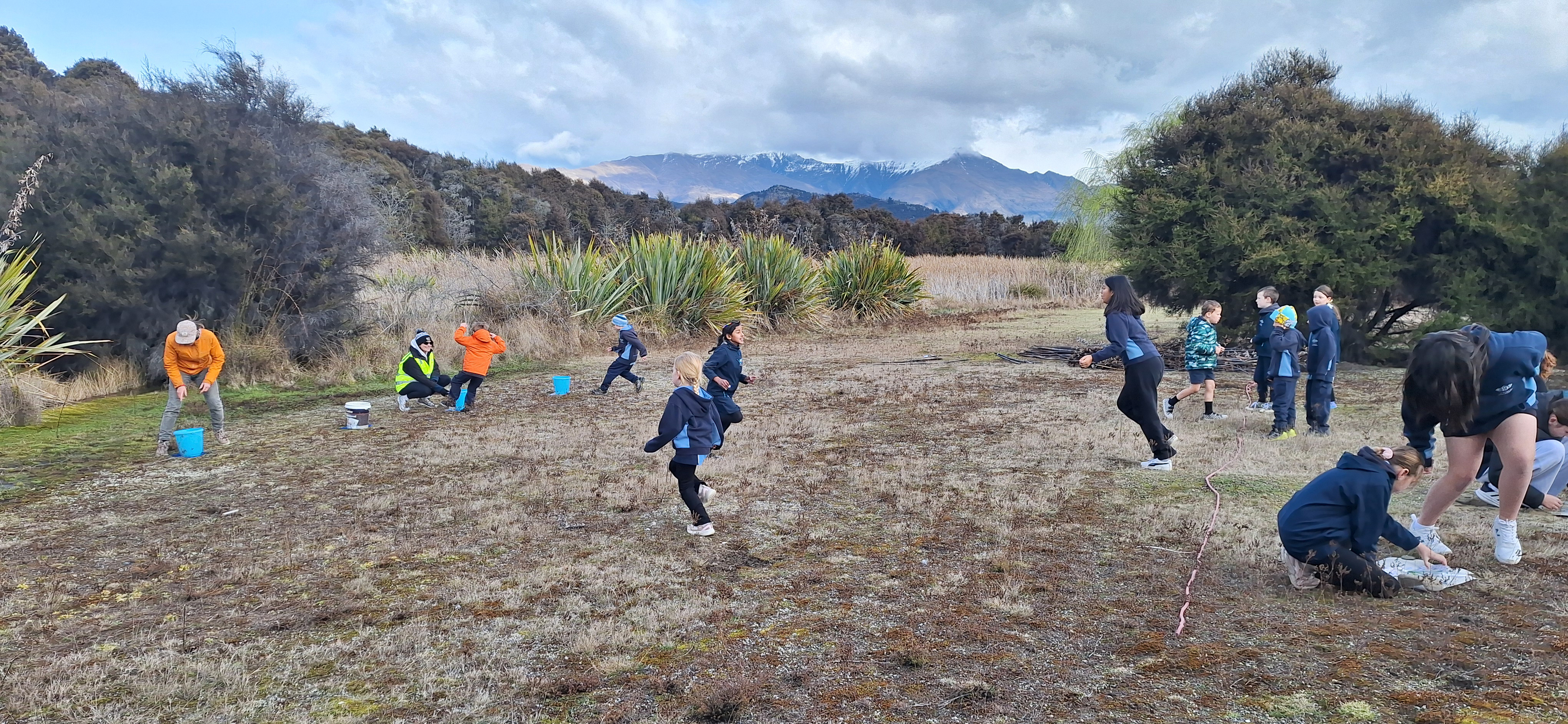 a group of school students and some adults in a rural clearing with native bush and trees around them