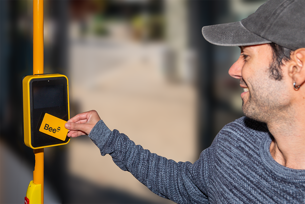 a person wearing a hat scanning a Bee Card while boarding a bus
