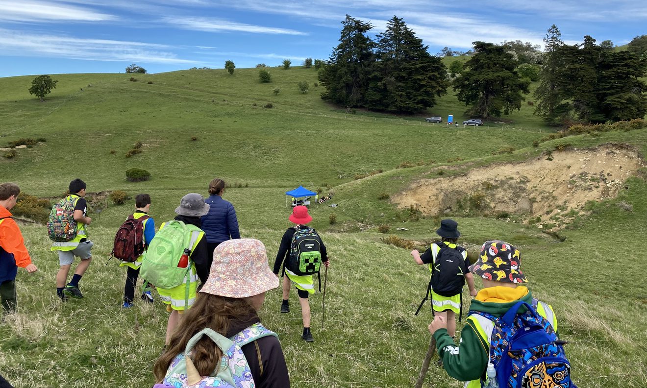 a group of children and an adult walking across a hill in a rural area