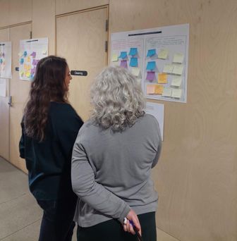 two people looking at a chart covered in sticky notes on a wall
