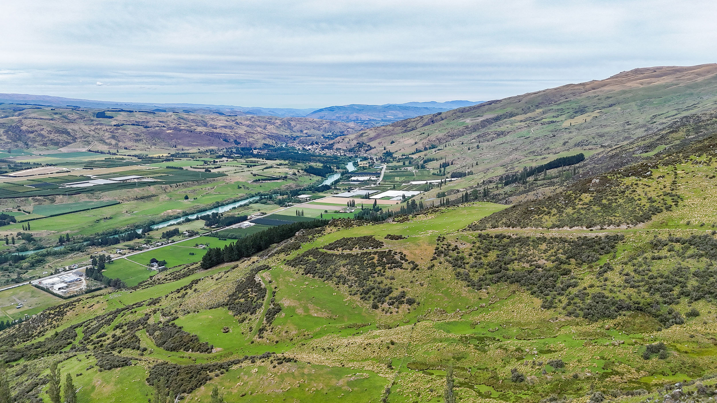 an aerial view of Roxburgh and the valley surrounded by hills with the Clutha River/Mata-Au running through the valley floor