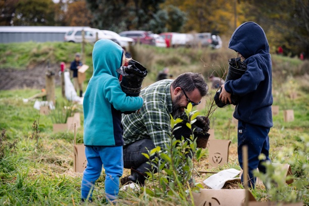 a man and two children planting plants along a riverbank