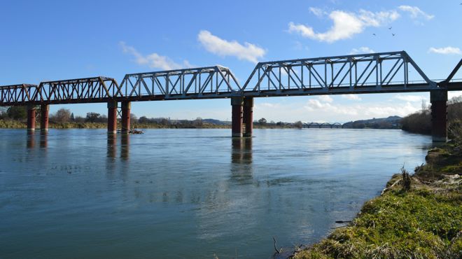 a rail bridge over a river with a blue sky