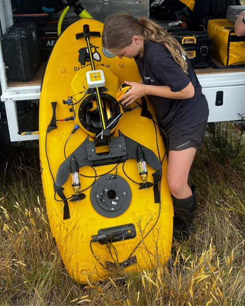 a person standing at the back of a vehicle holding a yellow boat-shaped piece of equipment