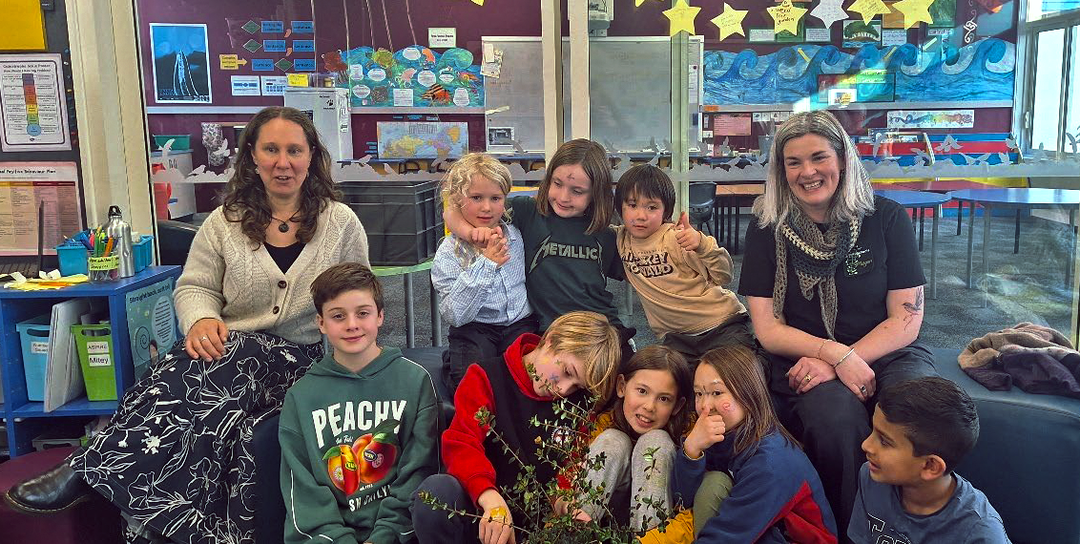 a group of children with two adults sitting in a classroom and looking at the camera