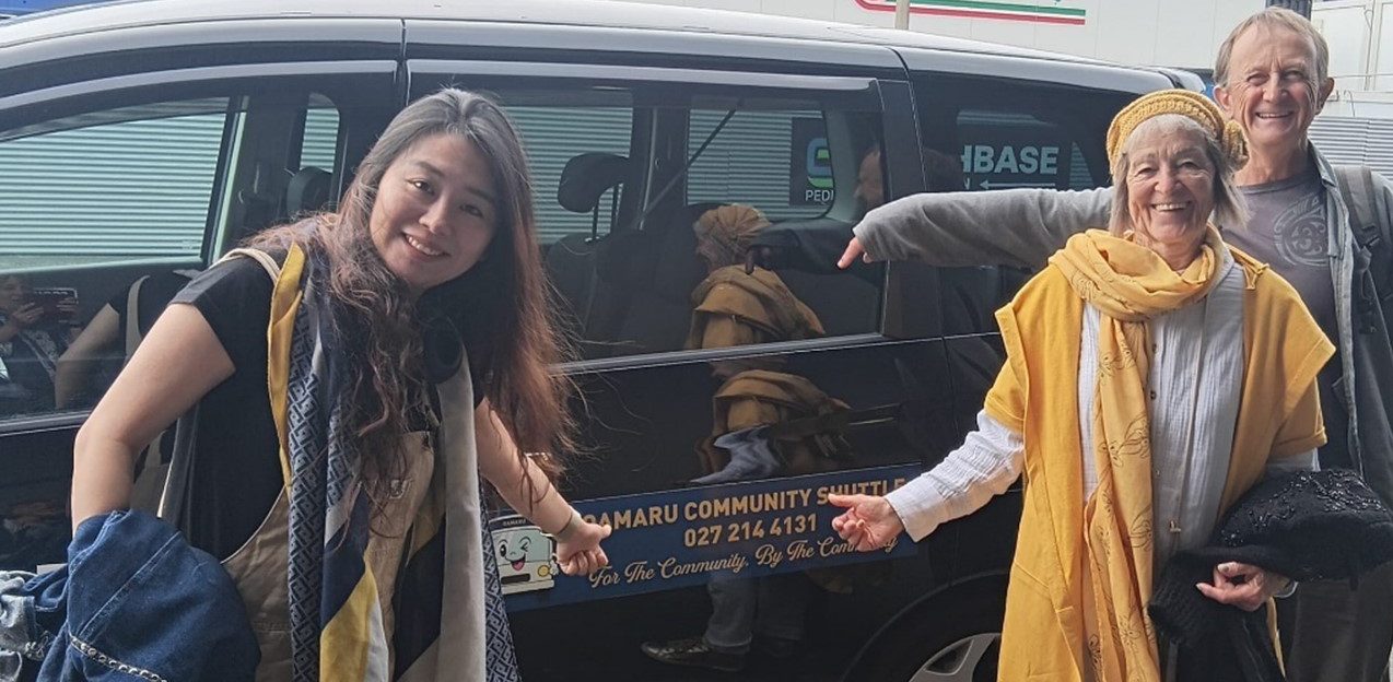 three smiling people standing beside a van smiling at the camera