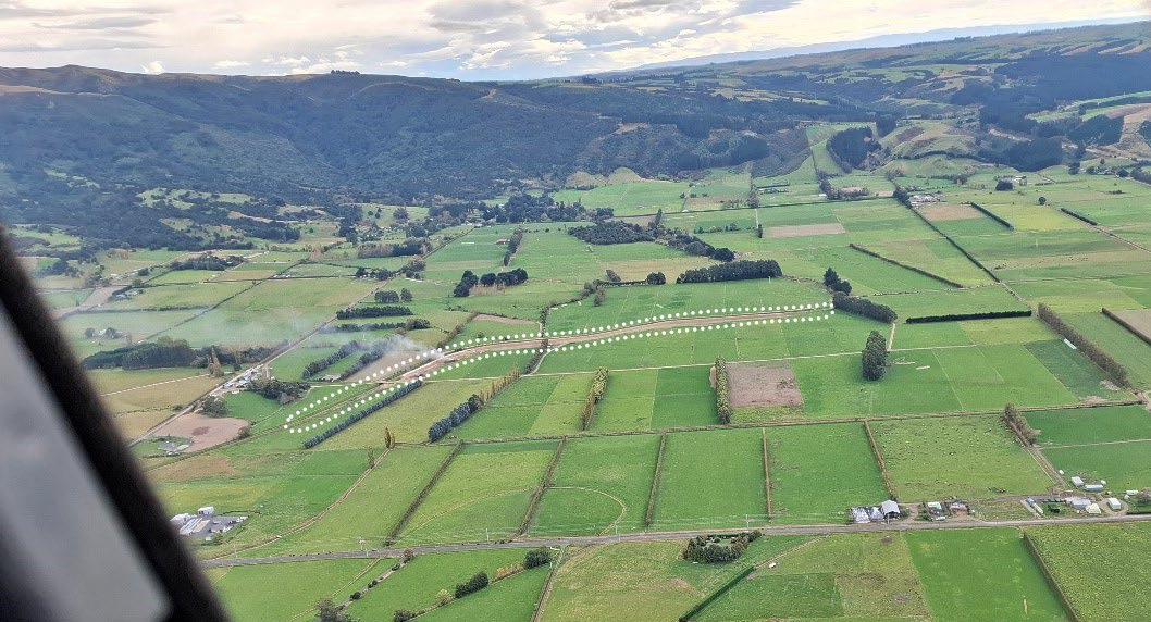 an aerial view of a flat rural area with hills in the background and a dotted line showing where a contour channel is
